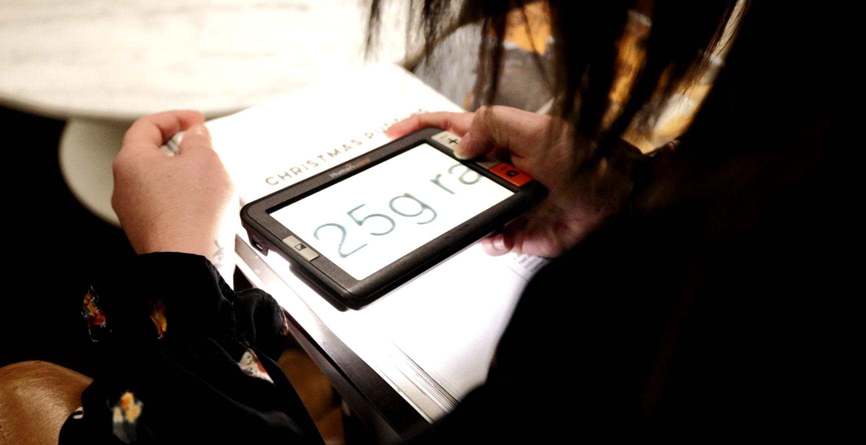 Electronic magnifier Person using a hand-held electronic magnifier device over a piece of paper. The text on paper is magnified on the hand-held device.
